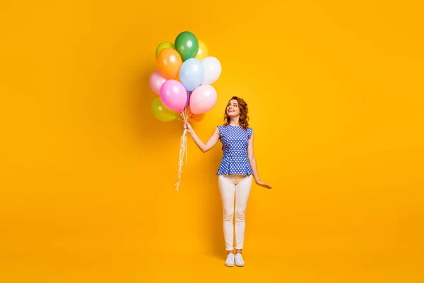 Foto in voller Größe lustige attraktive Dame halten viele bunte Luftballons Überraschung Geschenk kippen die Augen weg tragen Tupfen blaues Hemd weiße Hose Turnschuhe isoliert gelbe Farbe Hintergrund — Stockfoto