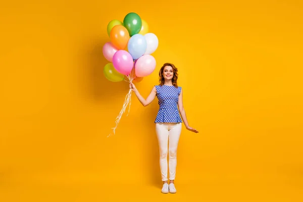 Фотографія красивої леді тримає багато різнокольорових повітряних кульок, які відвідують корпоративний захід, одягнені в синю сорочку з білими штанами, ізольовані жовтий кольоровий фон — стокове фото