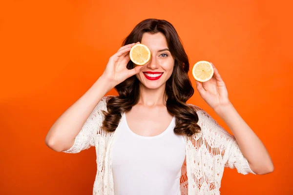 Foto de pelo castaño alegre positivo lindo encantadora novia bonita sonriendo juguetonamente ocultando su ojo detrás de la mitad de limón aislado sobre fondo de color vivo —  Fotos de Stock