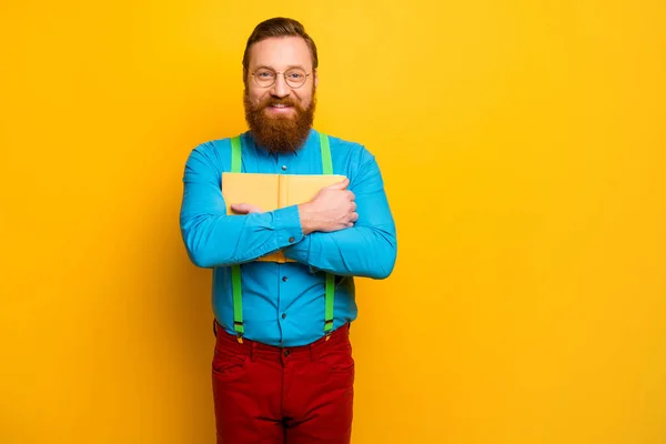 Photo of handsome attractive guy hold favorite book novel close chest imaginary flight inspiration wear blue shirt green suspenders red pants isolated yellow color background — Stok fotoğraf