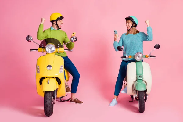 Full längd foto av millennial dam kille två personer sitta vintage moped semester kort sluta bläddra telefon läsa sms höja knytnävarna bära casual jumper headgear isolerad rosa färg bakgrund — Stockfoto