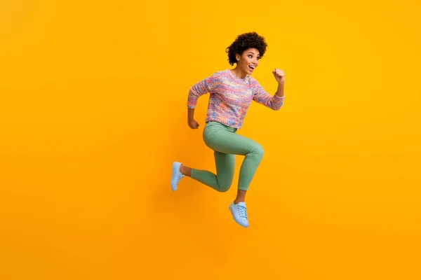 Полноразмерная фотография профиля веселой сумасшедшей смешной афроамериканской девушки, прыгающей быстро после скидки в черную пятницу, одетой в стильный зеленый наряд, изолированный сверкающим ярким цветовым фоном — стоковое фото