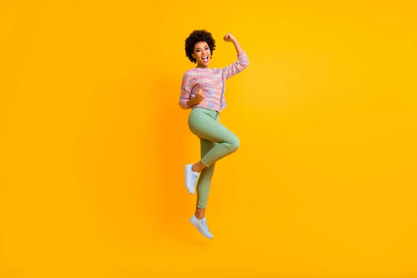 Foto de longitud completa de la chica afroamericana encantada salto celebrar ganar la lotería de otoño disfrutar de regocijo levantar los puños gritar sí usar suéter verde colorido aislado color amarillo fondo —  Fotos de Stock