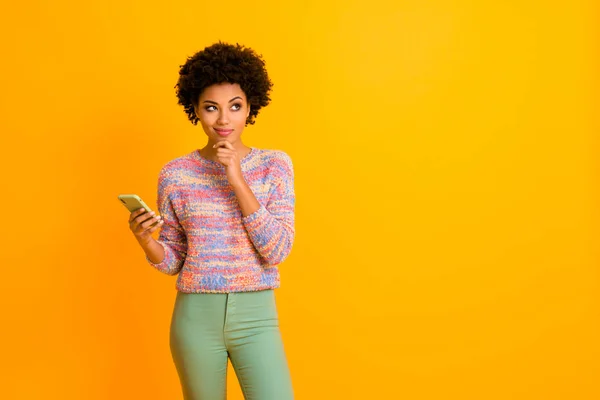 Portrét zájem snové afro americká dívka použít smartphone chtějí chatování myslet myšlenky hádat sociální média odpověď nosit zelené světlé kalhoty kalhoty izolované žluté barvy pozadí — Stock fotografie
