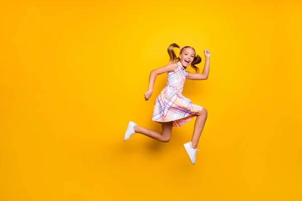 Full size profile side photo of cheerful crazy funny small kid girl jump run after spring time discount wear checkered skirt footwear isolated bright yellow color background — 스톡 사진
