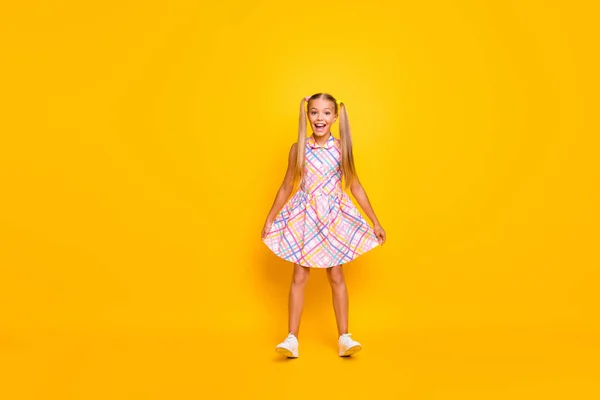 Full length photo of beautiful small lady good mood pretty long tails hold skirt stand on heels wear plaid summer dress white sneakers isolated yellow shine color background — Stok fotoğraf
