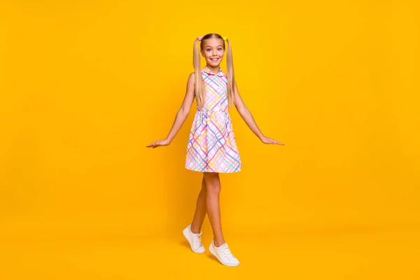 Full body photo of funny beautiful little lady good mood pretty long tails playful walk street wear plaid summer sun dress white sneakers isolated yellow shine color background — Stockfoto