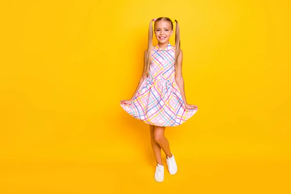 Full length photo of beautiful small lady hold sundress skirt hands good mood pretty long tails wear plaid summer dress white sneakers isolated yellow vibrant color background — Φωτογραφία Αρχείου