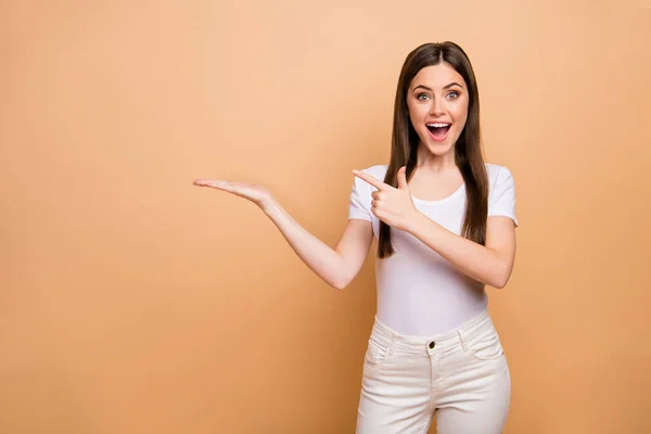 Portrait of astonished crazy girl hold hand point index finger recommend adverts suggest select promo wear white pants trousers isolated over beige color background — 图库照片