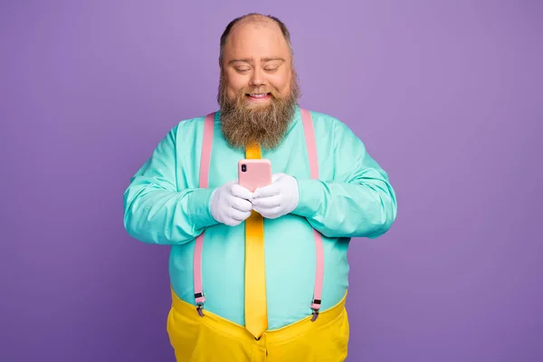 Retrato de positivo alegre homem gordo uso smartphone texting digitação leitura mídia social notícias desgaste teal camisa amarelo rosa calças calças isoladas sobre brilho cor violeta fundo — Fotografia de Stock