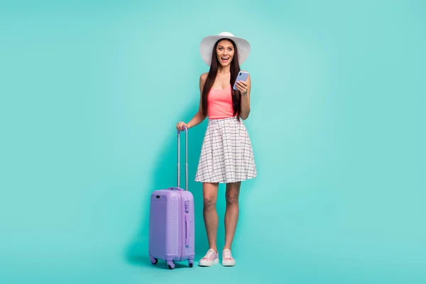 Full size surprised girl travel use smartphone impressed fast hotel reservation scream wow hold bag wear sunhat white checkered plaid skirt pink tank-top isolated turquoise color background — 图库照片