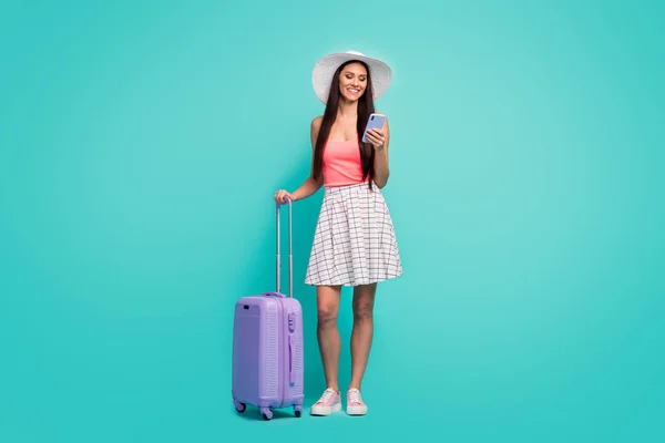 Full length photo positive girl arrive summer weekend resort use smartphone search book hotels hold trolley wear sunhat pink singlet white checkered plaid skirt isolated teal color background — 스톡 사진