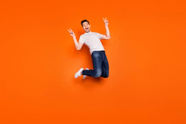 Полноразмерное фото позитивного веселого парня, прыгающего на весенних каникулах, заставляет v-sign носить стильный наряд в стиле casual, обувь на ярком цветовом фоне — стоковое фото