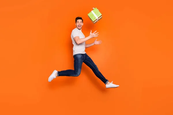Full length profile photo of crazy guy jump high up catch big green giftbox unexpected present wear striped t-shirt τζιν παπούτσια απομονωμένο φωτεινό πορτοκαλί χρώμα φόντο — Φωτογραφία Αρχείου