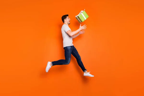 Perfil de corpo inteiro foto de cara engraçado saltar alto pegar grande caixa de presente verde sorte aniversário presente desgaste listrado t-shirt jeans tênis isolado cor laranja brilhante fundo — Fotografia de Stock