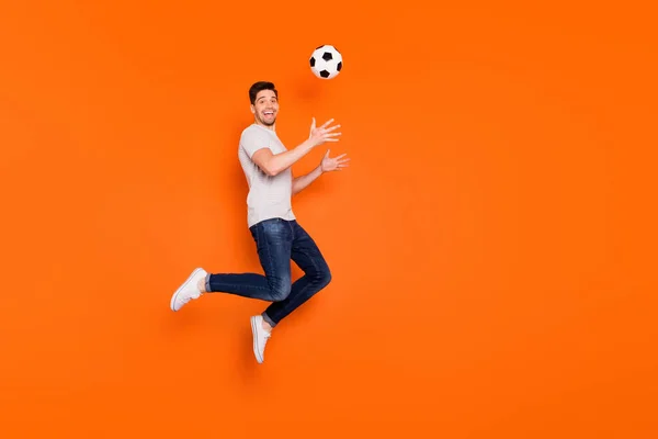 Полный профиль тела фото смешного парня прыгать высоко вверх поймать футбольный мяч зависимый фанат вратарь носить полосатые футболки джинсы кроссовки изолированные ярко-оранжевый цвет фона — стоковое фото