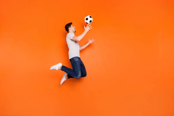Full size profil zdjęcie funky facet skakać wysoko w górę złapać piłka nożna uzależniony wentylator bramkarz nosić paski t-shirt dżinsy trampki izolowane jasny pomarańczowy kolor tła — Zdjęcie stockowe