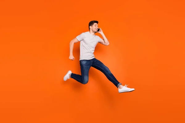 Foto de perfil de comprimento total do cara funky salto alto espera telefone apressando-se falar amigos reunião desgaste listrado t-shirt jeans tênis isolado cor laranja brilhante fundo — Fotografia de Stock