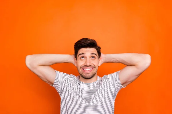 Foto de chico atractivo cogido de la mano detrás de la cabeza momento de relajación sonrisa dentada fin de semana por la mañana buscar espacio vacío desgaste rayas camiseta aislado color naranja brillante fondo — Foto de Stock