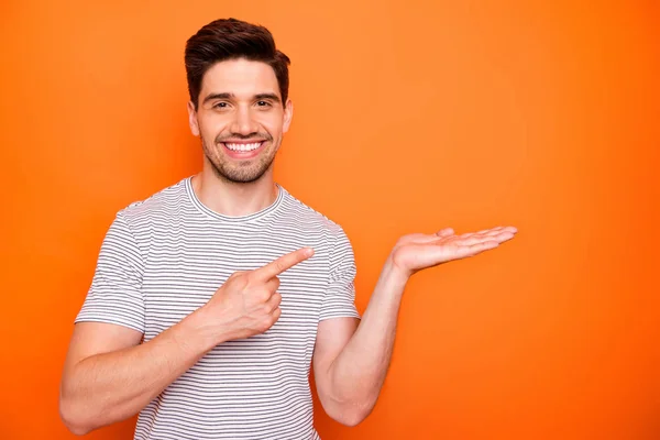 Foto av attraktiv kille hålla öppen handflata regissera finger nyhet rabatterat pris produkt råda försäljning shopping bära randig t-shirt isolerad ljus orange färg bakgrund — Stockfoto