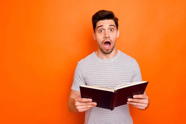 Foto av rolig attraktiv kille hålla favorit bok händer läsa spännande sista intriger öppen mun oväntade händer slitage randig t-shirt isolerad ljus orange färg bakgrund — Stockfoto