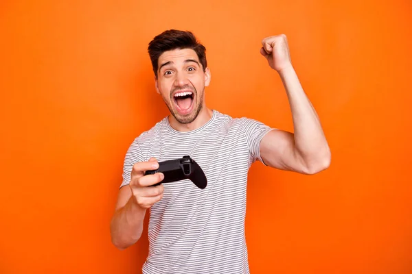 Photo de drôle fou étonné gars tenir la main joystick jouer à des jeux vidéo joueur excité est venu finir premier lever poing usure rayé t-shirt isolé couleur orange vif arrière-plan — Photo