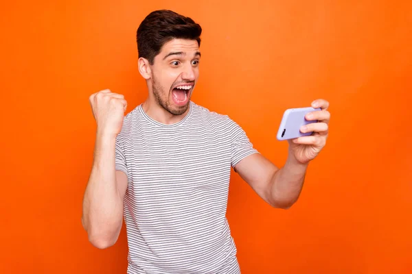 Doel. Foto van funky coole jongen vrolijk goed humeur hold telefoon raise vuist vieren succesvolle sport team spel dragen gestreept t-shirt geïsoleerde levendige oranje kleur achtergrond — Stockfoto