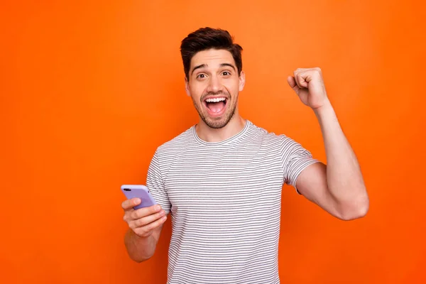 Photo of funky cool guy cheerful good mood hold telephone raise fist celebrate first startup successful income wear striped t-shirt isolated bright orange color background — Stockfoto