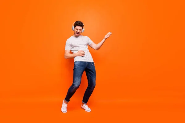 Full length photo of funky guy chilling listen modern earphones hold hands play imagine guitar rehearse wear striped t-shirt jeans shoes isolated bright orange color background — ストック写真