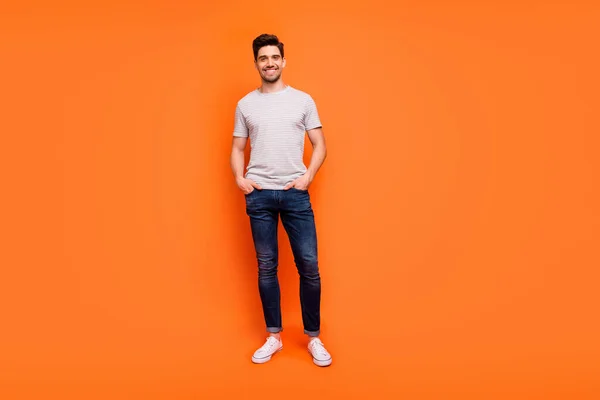 Full length photo of cool guy cheerful person street casual look clothes hands pockets toothy smile wear striped t-shirt jeans shoes isolated bright orange color background — Φωτογραφία Αρχείου