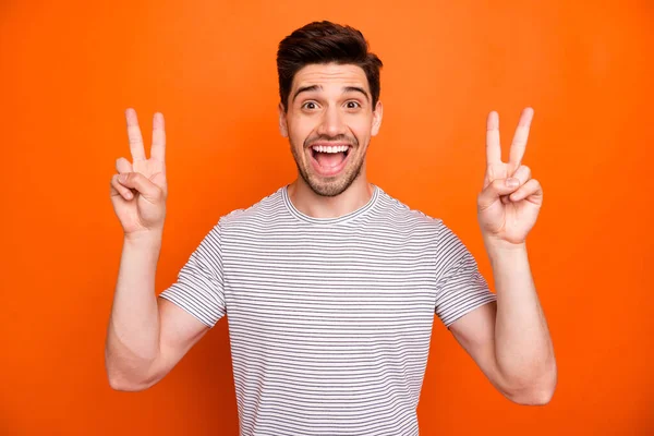 Photo of cool funny guy open mouth raise hands showing v-sign symbols cheerful person wear casual striped t-shirt isolated bright orange color background — 图库照片