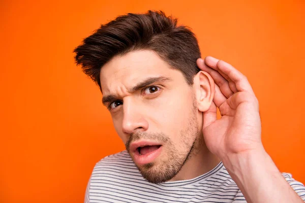 Closeup photo of silly crazy guy chatterbox hold arm near ear attentively listen friends telling secrets wear casual striped t-shirt isolated bright orange color background — Stockfoto