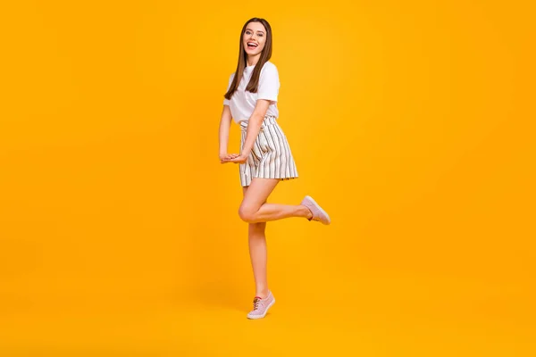 Full size profile photo of funny lady walking down street enjoy sunny day flirty mood wear casual white t-shirt striped shorts shoes isolated vibrant yellow color background — Stock Fotó