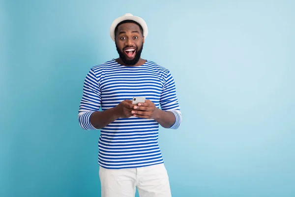 I see ocean. Photo of funny dark skin guy traveler good mood hold telephone app chatting friends wear white sun cap striped sailor shirt shorts isolated blue color background — Stok fotoğraf