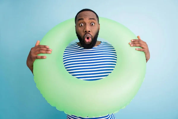 Photo of funny speechless dark skin guy hold green life buoy ready swim ocean sea traveler see sale banner advert not believe eyes wear striped sailor shirt isolated blue color background — Zdjęcie stockowe
