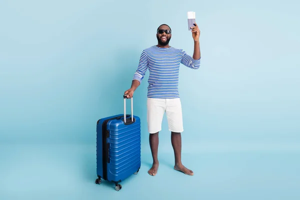 Полная длина фото положительный смешной афро-американец мужчина туристические документы держать тележки пользуются отдыха выходные носить солнцезащитные очки полосатый жилет белые шорты изолированы синий цвет фона — стоковое фото