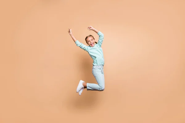 Full body profile photo of beautiful funny little lady jumping high up cheerleader celebrating winning raise fists wear blue sweater jeans footwear isolated beige color background