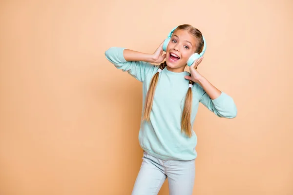 Foto de hermosa señorita divertida disfrutar escuchar auriculares inalámbricos frescos canción favorita buen humor boca abierta desgaste pantalones vaqueros de jersey azul aislado beige pastel color fondo —  Fotos de Stock