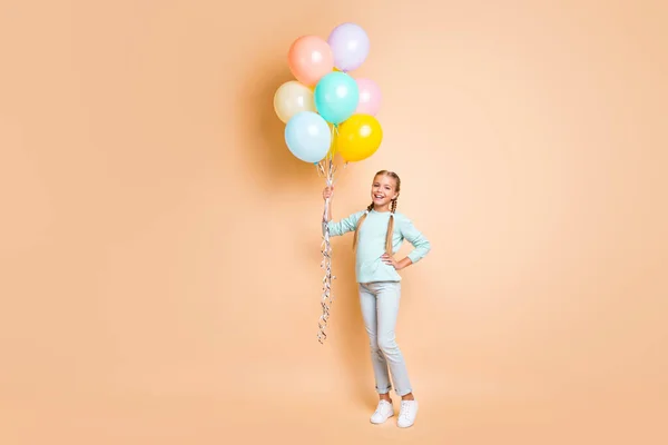 Foto de longitud completa de hermosa señora bastante pequeña sostienen muchos globos de aire soñadoras trenzas largas divertidas usan pantalones vaqueros de jersey azul zapatillas aisladas beige pastel color fondo —  Fotos de Stock