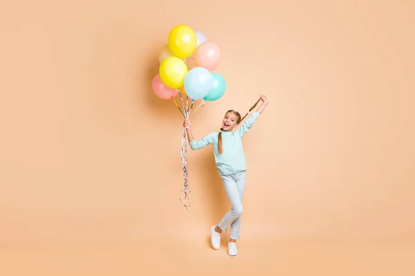 Full length photo of beautiful small lady many air balloons raise up long braid greeting best friend classmate wear blue sweater jeans sneakers isolated beige pastel color background — Stock Fotó
