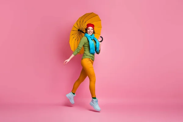 Full size photo of cheerful sweet cute girl jump enjoy go walk hold bright parasol wear blue red headwear sweater trousers footwear isolated over pink color background — Stockfoto