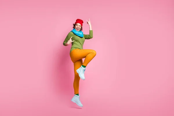 Full size photo energetic girl jump enjoy rejoice spring sales rock and roll concert make horned symbol scream wear red blue yellow green shoes pants headwear isolated pink color background — Stok fotoğraf