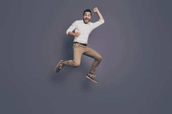 Full length photo of young handsome business man jumping high up rejoicing celebrating new startup project success wear white shirt pants footwear isolated grey color background