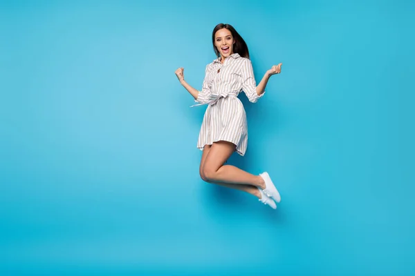 Full length profile photo of funny lady jump high rejoicing celebrate summer weekend vacation beginning wear spring striped mini dress footwear isolated blue color background — Zdjęcie stockowe
