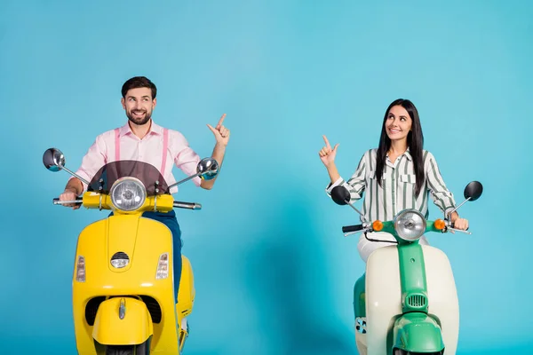 Positive cheerful two people bikers ride fast speed electric scooter follow way to journey point index finger copyspace wear striped pink shirt isolated over blue color background