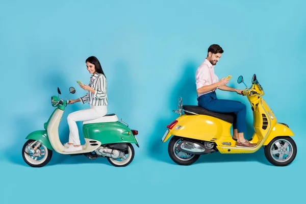 Full length profile side photo of positive two people bikers driver drive yellow green choppers use cellphone search gps location wear trousers shirt isolated blue color background