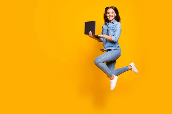 Full length profile photo of funny business lady jump high up hold notebook hands addicted worker always online wear casual denim outfit white sneakers isolated yellow color background — 스톡 사진