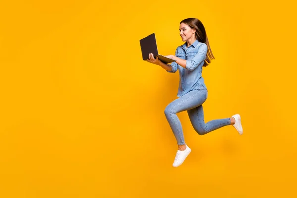Full size profile photo of beautiful business lady jump high hold notebook hands hurry work browsing laptop wear casual denim outfit white sneakers isolated yellow color background — 스톡 사진
