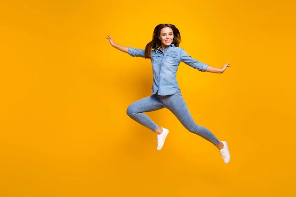 Full length photo of pretty funky lady jump high up rejoicing good mood spend weekend free time wear casual denim outfit white footwear isolated yellow color background — ストック写真