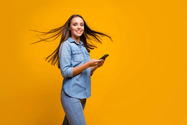 Profile photo of pretty lady hold telephone hands walk street hairdo flying addicted user modern technology user wear casual jeans denim outfit isolated yellow color background — Zdjęcie stockowe